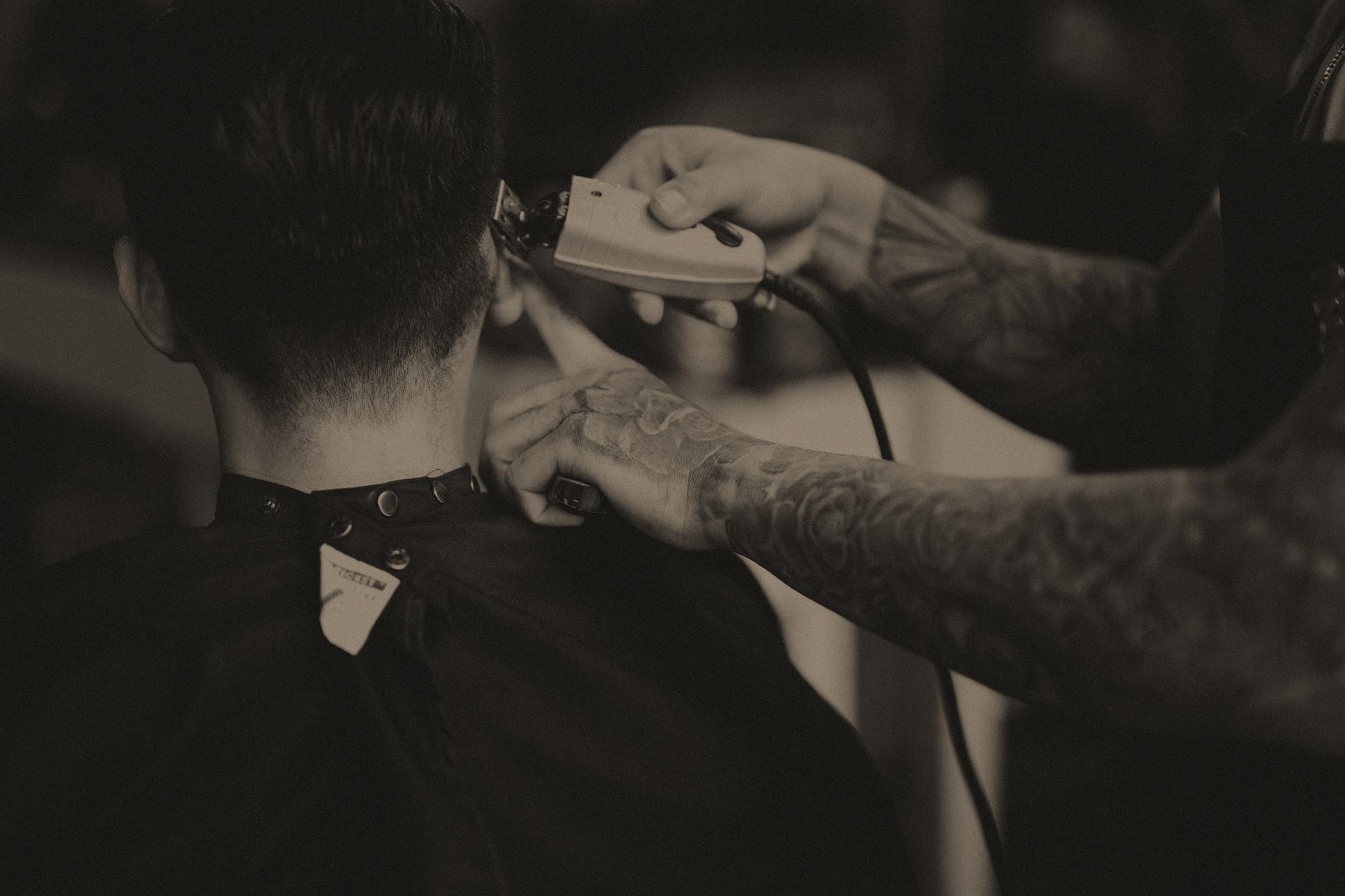 Barber mit tätowierten Armen setzt den Clipper im Nacken an