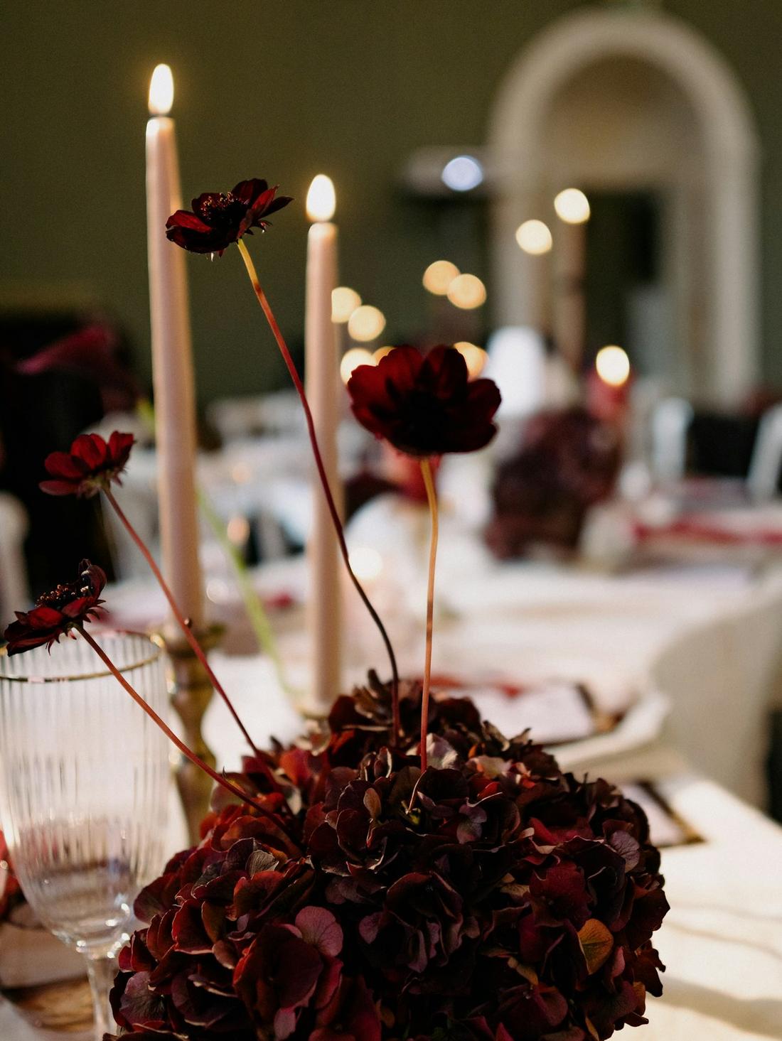 Hohe Kerzen und dunkle Blumen auf einem gedeckten Tisch