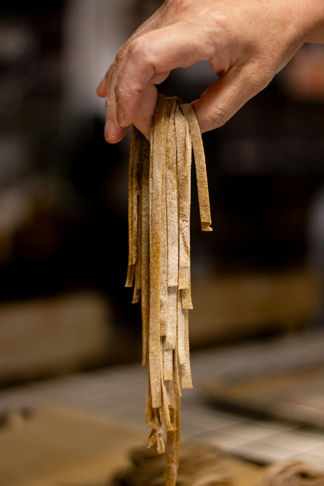 Hände heben frische Pasta aus Mehl